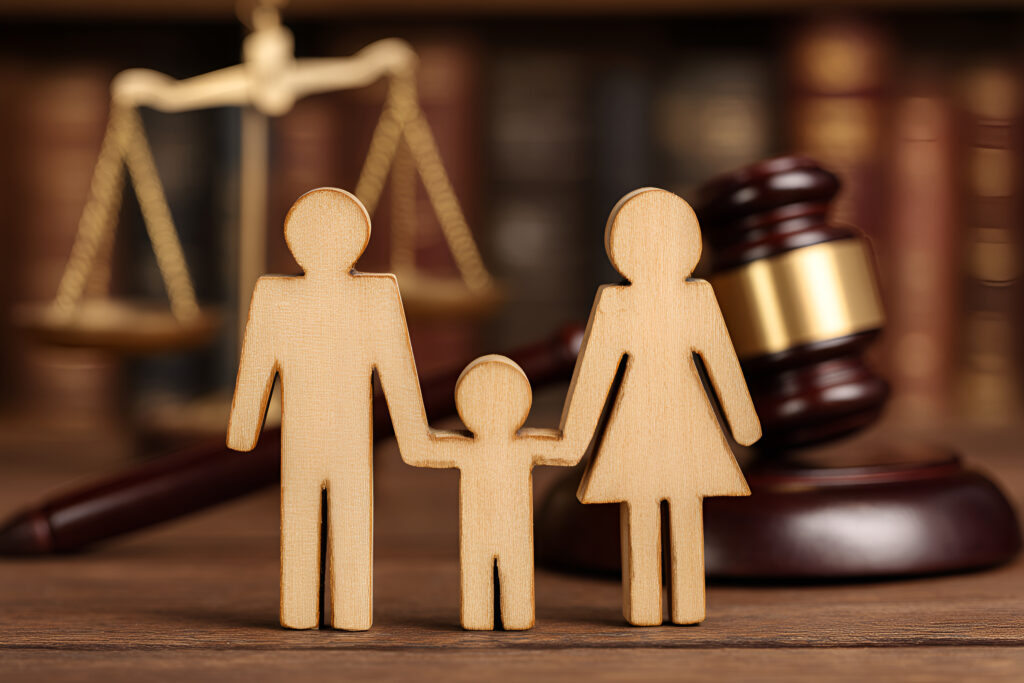 Figuras de madera que representan a una familia se toman de las manos junto a un mazo y una balanza de la justicia, simbolizando el derecho de familia y los procesos legales relacionados con asuntos familiares.